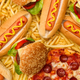 Hot dogs, burgers, and pizza laid haphazardly on a background of french fries